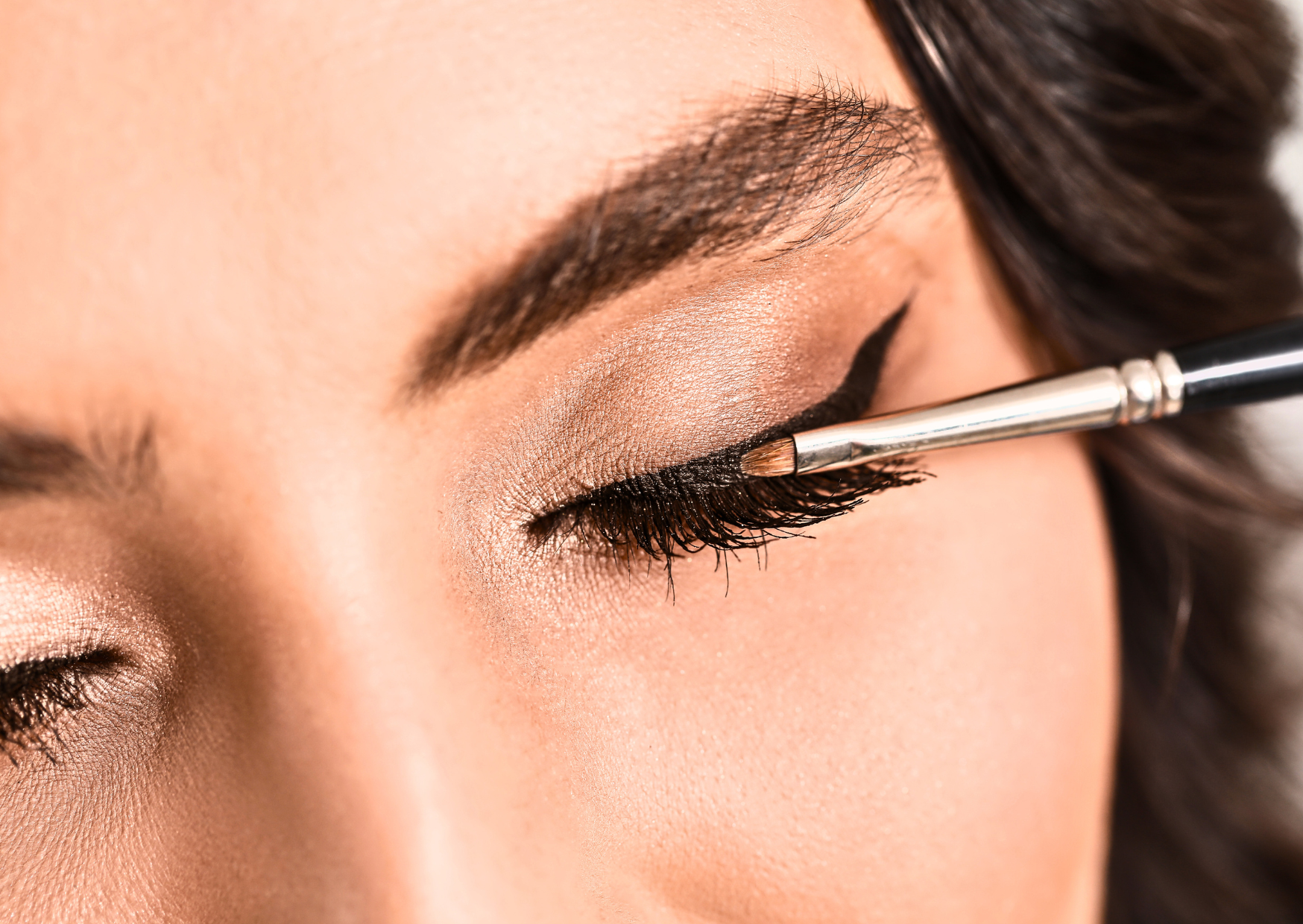 A woman strategically applying black eyeliner to her top lid to enhance the shape of her eyes