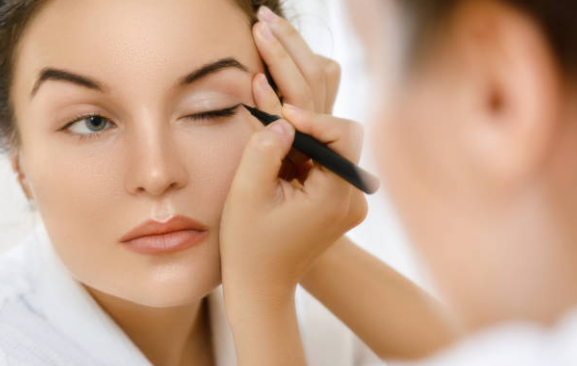 oung woman applying eyeliner to upper lid for eye makeup tutorial